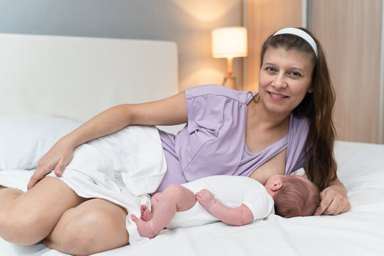 ..Mother with eldest daughter and  newborn baby feeds her breasts with mother's milk in the bedroom on the bed at home
