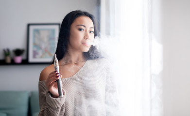 Casual asian woman vaping electronic cigarette at home