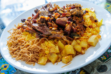 Plate of yellow rice topped with mutton meat and potatoes.