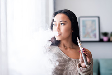 Casual asian woman vaping electronic cigarette at home