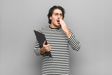 Young employee man holding an inventory yawning showing a tired gesture covering mouth with hand.