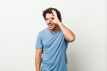 Young handsome man against a white background excited keeping ok gesture on eye.