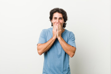 Young handsome man against a white background laughing about something, covering mouth with hands.