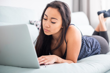 Relaxed asian girl using laptop sitting on sofa at home