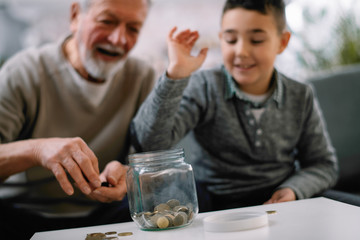 Obraz na płótnie Canvas Grandpa and grandson saving money. Grandfather teaching grandchild how to save money. 