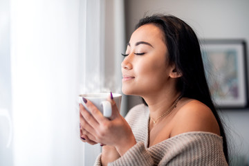 Relaxed asian woman with cup of tea or coffee spending leisure time at home