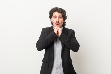 Young business man against a white background praying for luck, amazed and opening mouth looking to front.