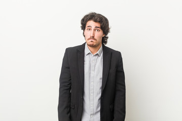 Young business man against a white background shrugs shoulders and open eyes confused.