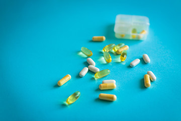 Vitamins and pills on a blue background in rows with a pill box. Omega Capsules and White Yellow Vitamins