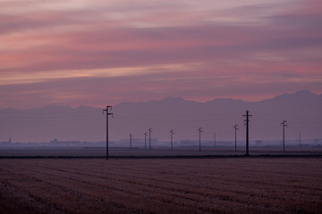 Obraz premium Sunset landscape in the countryside with power line, poles and old farms in the Piedmont plain, Po valley, Italy
