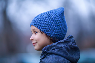 Curly boy on blue knitted hat looks away
