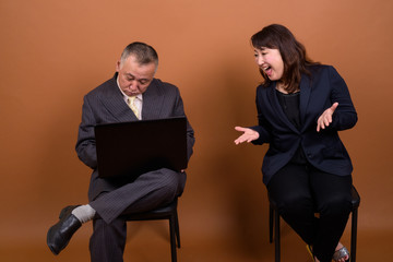 Mature Asian businesswoman with mature Asian businessman using laptop