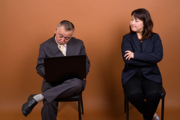 Mature Asian businesswoman with mature Asian businessman using laptop