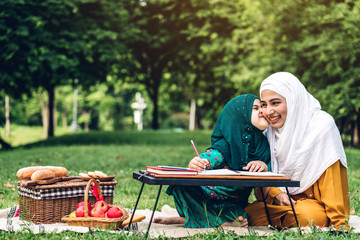 Portrait of happy muslim mother and little muslim girls child learning together with hijab dress smiling and enjoy relax reading and write a book in summer park.Education concept