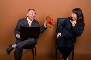 Obraz premium Mature Asian businesswoman with mature Asian businessman using laptop