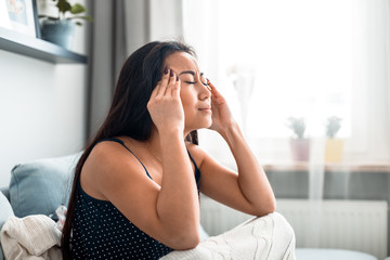 Upset depressed asian girl on couch suffering from headache migraine