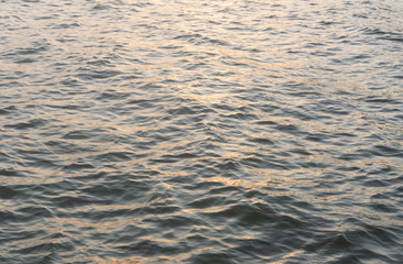 Water ripple surface reflection effect from sunset and sky top view at lake in evening day,wave abstract texture sunlight black and golden pattern background