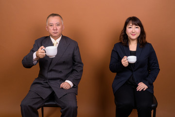 Mature Asian businessman and mature Asian businesswoman drinking coffee together