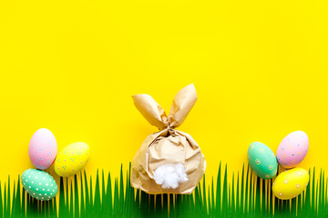 Easter concept. Eggs, decorative bunny and grass on yellow background top-down copy space