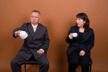 Mature Asian businessman and mature Asian businesswoman drinking coffee together