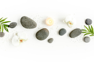 Spa stones, palm leaves, flower white orchid, candle and zen like grey stones on white background. Flat lay, top view - obrazy, fototapety, plakaty