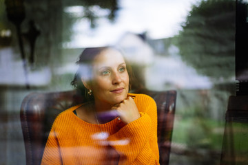 Young woman sits in a leather armchair behind a window and looks into the camera