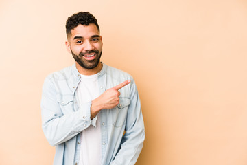 Young mixed race arabic man isolated smiling and pointing aside, showing something at blank space.