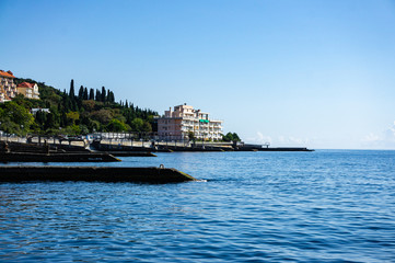 Yalta, Russia - September 30, 2019: View of coastline with breakwaters and hotels along shore against background of Crimean mountains. Selective focus. Clear sea is dark blue.