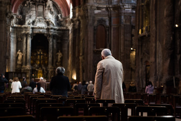 Interior of old church in Lisbon. People praying at mass. A ray of sunshine enters through the...