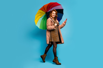 Full body profile side photo positive emotions woman go walk enjoy use smartphone read social media news hold umbrella shield wear beige shoes tights stockings isolated blue color background