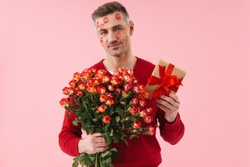 Portrait of man with kiss marks at his face holding flowers and gift box