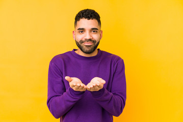 Young mixed race arabic man isolated holding something with palms, offering to camera.