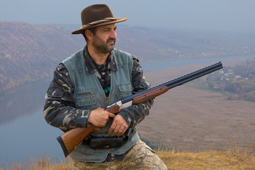 Fototapeta premium Hunter man in camouflage with a gun during the hunt in search of wild birds or game. Autumn hunting season.