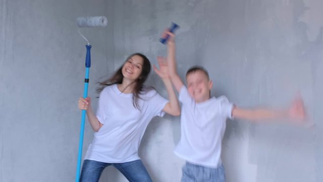 Family mom and son playing, jumping and aping with paint rollers painting wall. Mother making renovation and construction works at home, apartment, flat their selves. Woman and child boy painters.