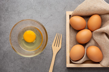 Chicken eggs on the wooden tray, fork and glass bowl on the black cement floor. Top view.