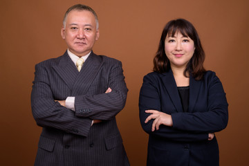 Mature Asian businessman and mature Asian businesswoman with arms crossed together