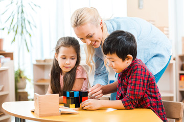 Smiling teacher playing building blocks with kids during lesson in montessori class