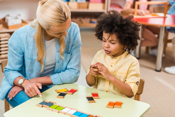 African american child playing educational game by teacher at table in montessori class