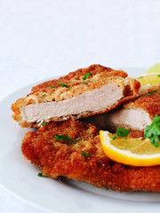 Wiener Schnitzel cut in two served with lemon slices and parsley leaves over white, verical