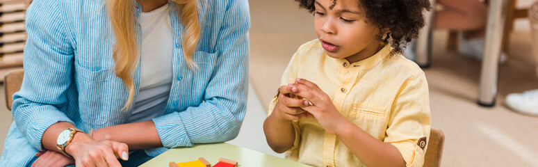 Panoramic shot of african american kid playing educational game by teacher in montessori school