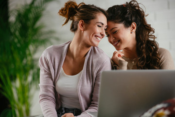 Two friend sitting on couch with laptop and listening music. Sisters having fun. 