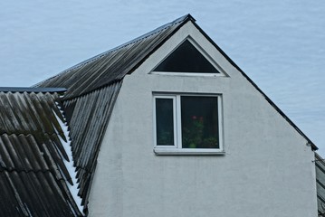 part of a private house with an attic with a gray wall and a window under a slate roof against the sky in a winter day