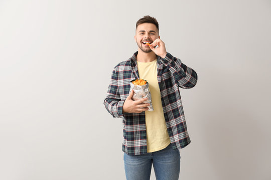 Handsome Young Man With Tasty Potato Chips On Light Background