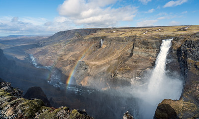 Panorama of Haifoss waterfall in the Icelandic highlands during blue cloudy sky with rainbow. The valley and the river leads the eye towards the wilderness. Traveling concept.