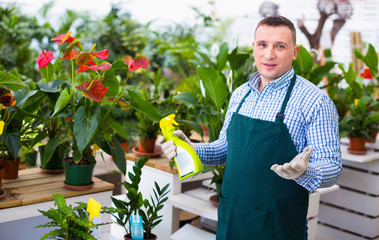 Man gardener is demonstraiting substances for care of flowers in greenhouse.