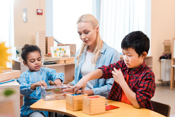 Selective focus of kids playing educational games by teacher in montessori school