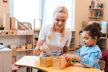 Smiling teacher playing wooden game with child during lesson in montessori school