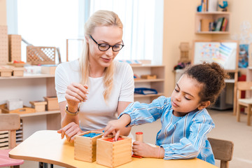 Teacher and kid folding wooden game at desk in montessori school