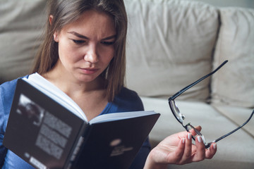 A woman with vision problems is reading a book with glasses.