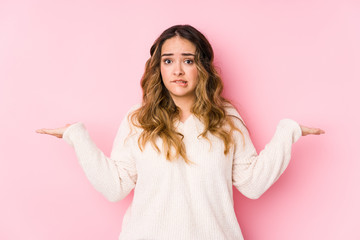Young curvy woman posing in a pink background isolated confused and doubtful shrugging shoulders to...